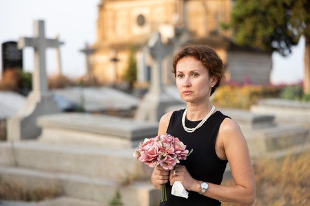 Woman in black dress with bouquet of flowers came to cemetery to honor the memory of deceased loved oneの写真素材