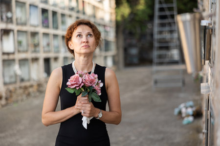 Drieving woman in black dress standing with bouquet by columbariumの写真素材