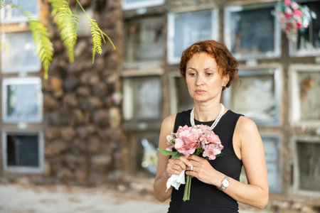 Sorrowful woman in black standing in cemetery with flowersの写真素材
