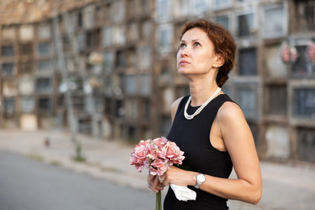 Sorrowful woman in black standing in cemetery with flowersの写真素材