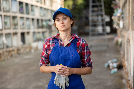 Young female cemetery employee stands with cloth work gloves in handsの写真素材