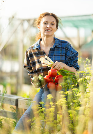 Woman shows off her harvest of zucchini, red tomatoes and green onions