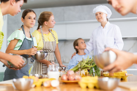 Children are excited to learn how to beat raw eggs with whisk under the guidance of female chefの写真素材