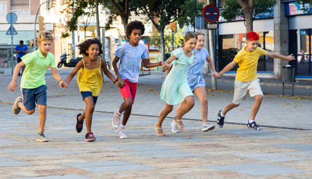 Happy children running together hand in hand through streetsの写真素材