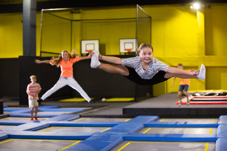 Cheerful girl bouncing spreading her legs on trampolines during free time on weekends at...