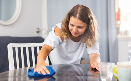 Positive brunette woman cleaning table at homeの写真素材