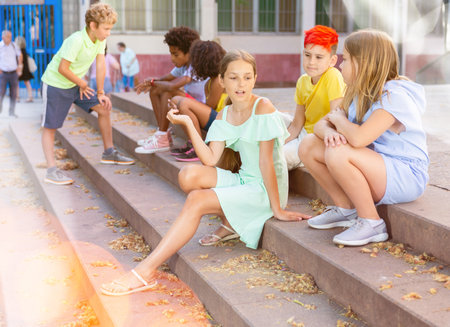 Cheerful preteen girls and boys sitting on steps outdoors and chattingの写真素材