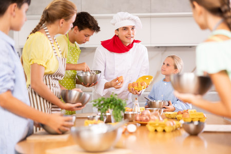 At cooking course, man cook with egg tray in hands tells children about cooking fluffy pancakesの写真素材