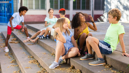 Happy tweenagers friends sitting on steps outdoors and chattingの写真素材