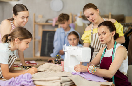 Seamstress explaining sewing techniques to schoolchildren in training workshopの写真素材