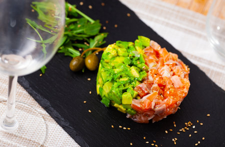 Salmon tartare with avocado and capers served on tableの写真素材