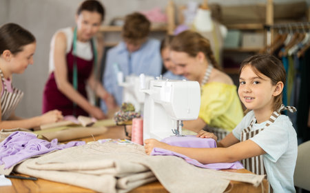 Tween schoolgirl stitching fabric on machine in school tailoring workshopの写真素材