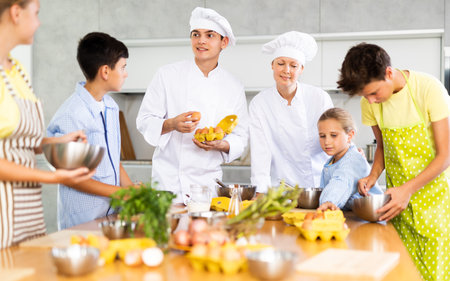 Man and woman cooks, during culinary master class, tell children rules when preparing doughの写真素材