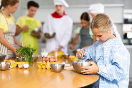 During cooking classes, girl carefully mixes ingredients in bowl with whisk.の写真素材