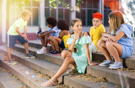 Children talking together while sitting on stairs outdoorsの写真素材