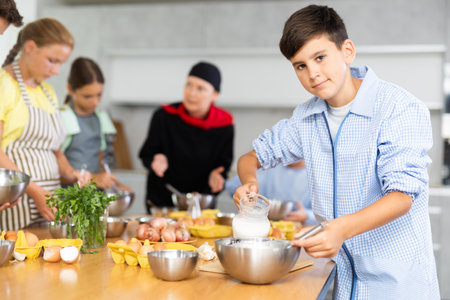 During cooking classes, teen boy carefully mixes ingredients in bowl with whiskの写真素材
