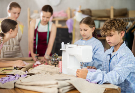 Preteen boy working at machine during group sewing course for kidsの写真素材