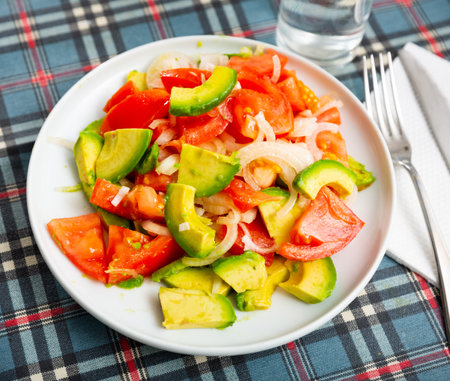 Tomato, avocado, onion salad served on tableの写真素材