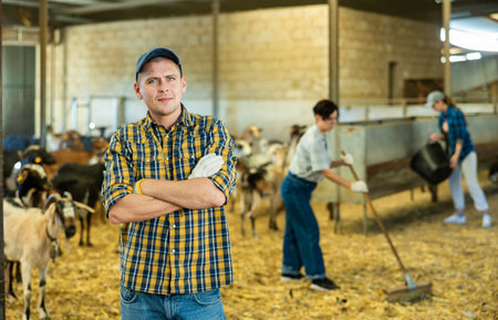 Confident positive farmer breeding dairy goats posing in shedの写真素材