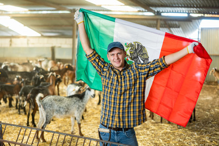 Excited young man holding flag of Mexico at goat barn
