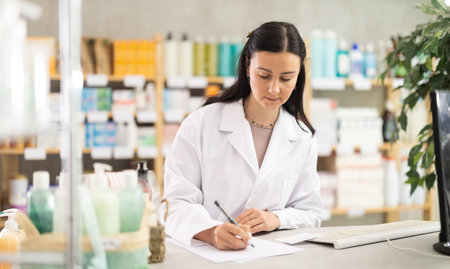 Middle-aged female pharmacist restocking with paper in drugstoreの写真素材