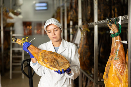 Satisfied female worker at jamon factory shows off finished jamonの写真素材