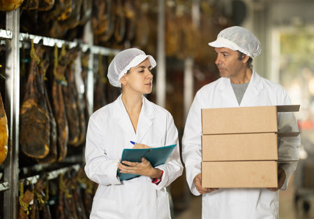 Woman head of department communicates with male porter at ham production factory