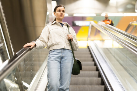 Woman metro passenger on escalator, enters underground public transport stationの写真素材