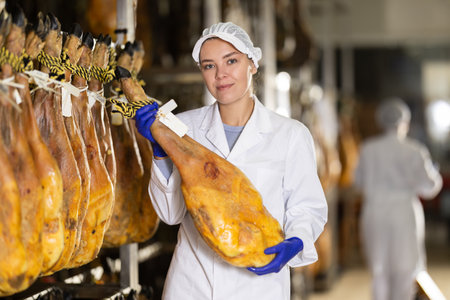Satisfied female worker at jamon factory shows off finished jamonの写真素材
