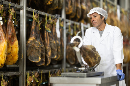 Man employee of hamon manufacturing workshop presents product using jamoneroの写真素材