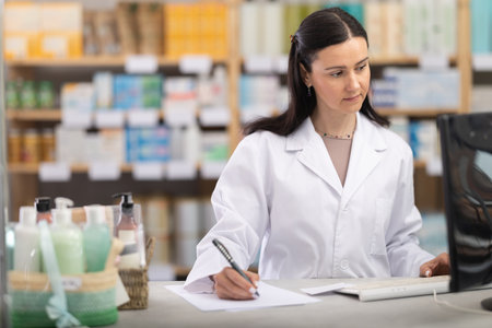 Female pharmacist working at computer and filling out papersの写真素材
