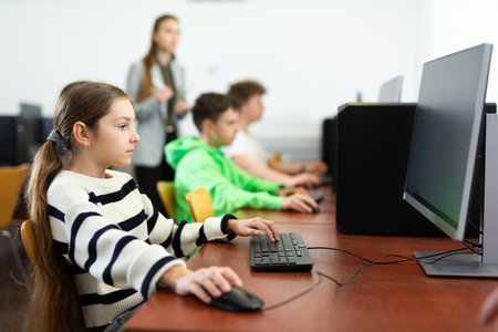 Pupils using computers at lesson, teacher teaching them in class roomの写真素材