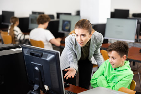 Frustrated teacher talking to careless preteen schoolboy in computer classの写真素材