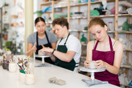 Young woman teacher helps teenagers boy and girl to sculpt ceramic productの写真素材