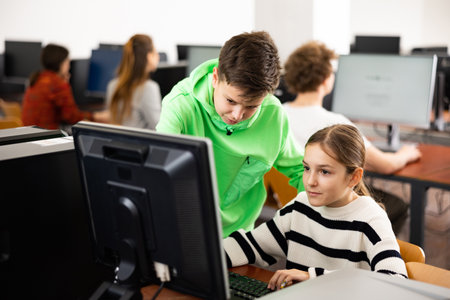 Teenage boy helping young girl with PC problem in computer classの写真素材