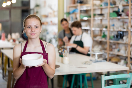 Teenage girl posing with ceramic bowl in ceramic workshopの写真素材