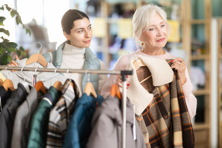 Family shopping concept. Two happy women choosing coat or jacket for cold season in clothing shop with large assortmentの写真素材