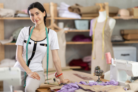 Female dressmaker sitting on table in sewing studioの写真素材