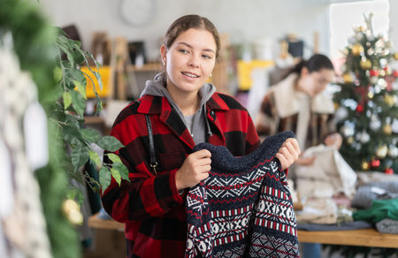 Woman is standing in a store and choosing a sweater against the background of a Christmas treeの写真素材