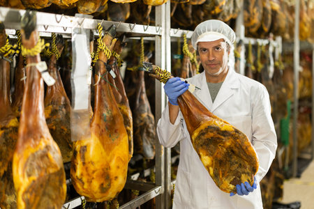 Satisfied male worker at jamon factory shows off finished jamonの写真素材