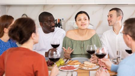 Middle-aged friends sitting at table with a glass of wine while having friendly conversationの写真素材
