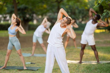 Fitness, sport and healthy lifestyle concept: group of multinational people doing yoga yoga pose - vrikshasana pose on mat in parkの写真素材