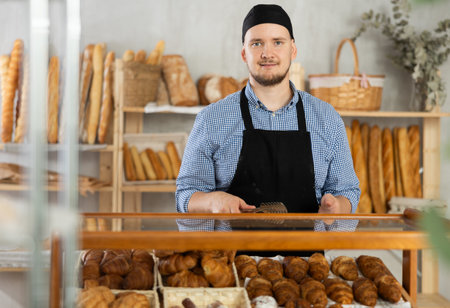 Man seller stands near window with bread and pastries at bakeryの写真素材