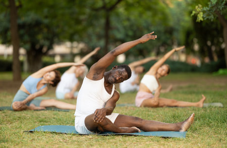 African American stretching in Parivrtta Janu Sirsasana during group yoga in parkの写真素材