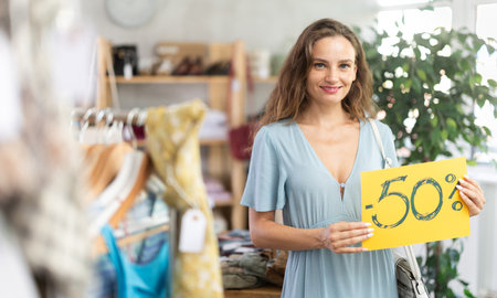 Young woman holding discount sign in clothing storeの写真素材
