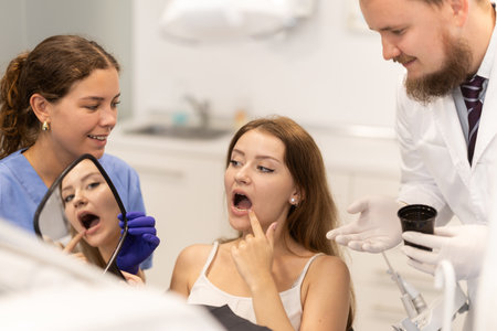 Male dentist helps a woman look at her repaired teeth in mirrorの写真素材