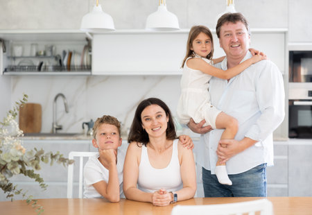 Parents posing with their two little children by the table in the kitchenの写真素材