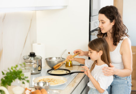 Happy mother and daughter frying pancakes in the kitchenの写真素材