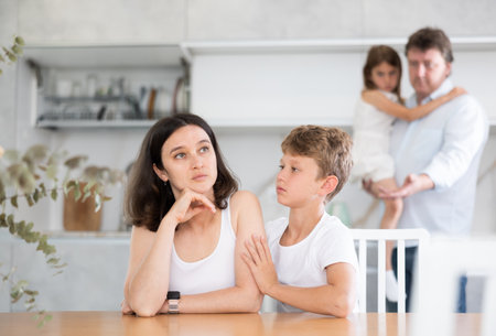 Son soothe his mother after a domestic quarrel. Father with little daughter in backgroundの写真素材