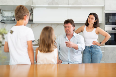At home in kitchen, outraged mom and dad scold their son and daughter for disobedience.の写真素材